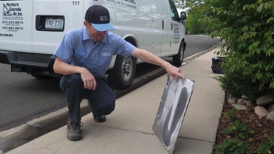 Northern Colorado Air technician inspecting a removed AC unit panel during an air conditioning repair service.